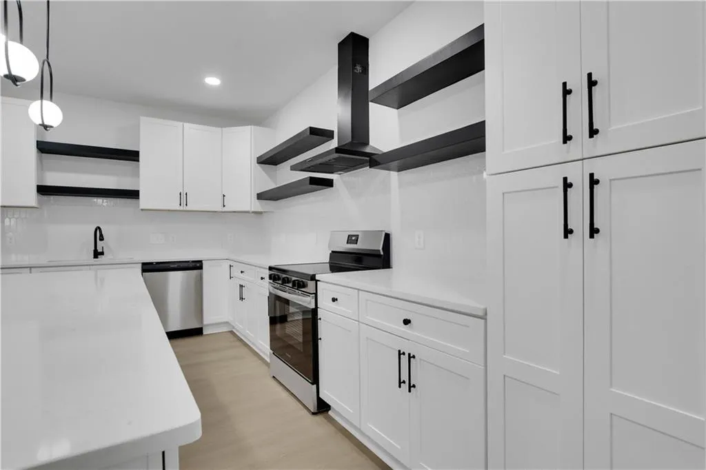 Kitchen with open shelves, appliances with stainless steel finishes, white cabinets, wall chimney exhaust hood, and decorative light fixtures