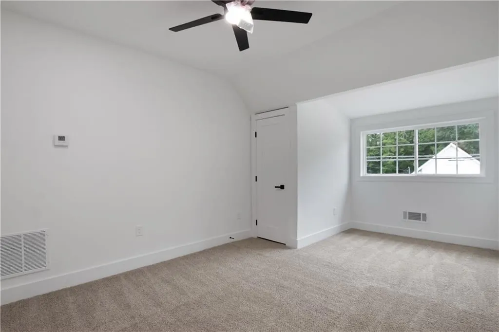 Empty room featuring vaulted ceiling, light carpet, and a ceiling fan