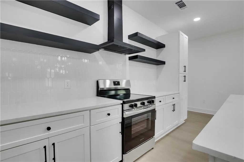Kitchen featuring open shelves, stainless steel range with electric stovetop, white cabinets, wall chimney exhaust hood, and light wood-style flooring