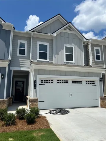 Contemporary townhouse exterior featuring a two-car garage with decorative hardware, a covered entry with a dark-frame glass door, brick accents, and board and batten siding