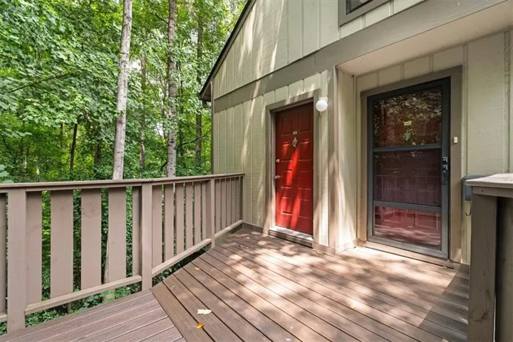 Wood-finish deck with a matching railing, two entry doors, and mature trees in the background