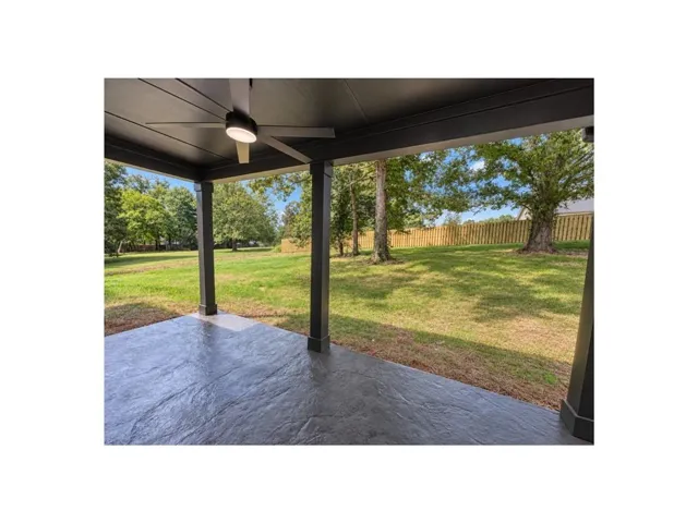 Covered patio with stamped concrete flooring, exposed beam ceiling, ceiling fan, and fenced backyard