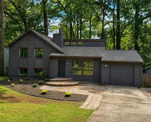 Contemporary home with dark gray siding, an attached garage, and a paver stone patio