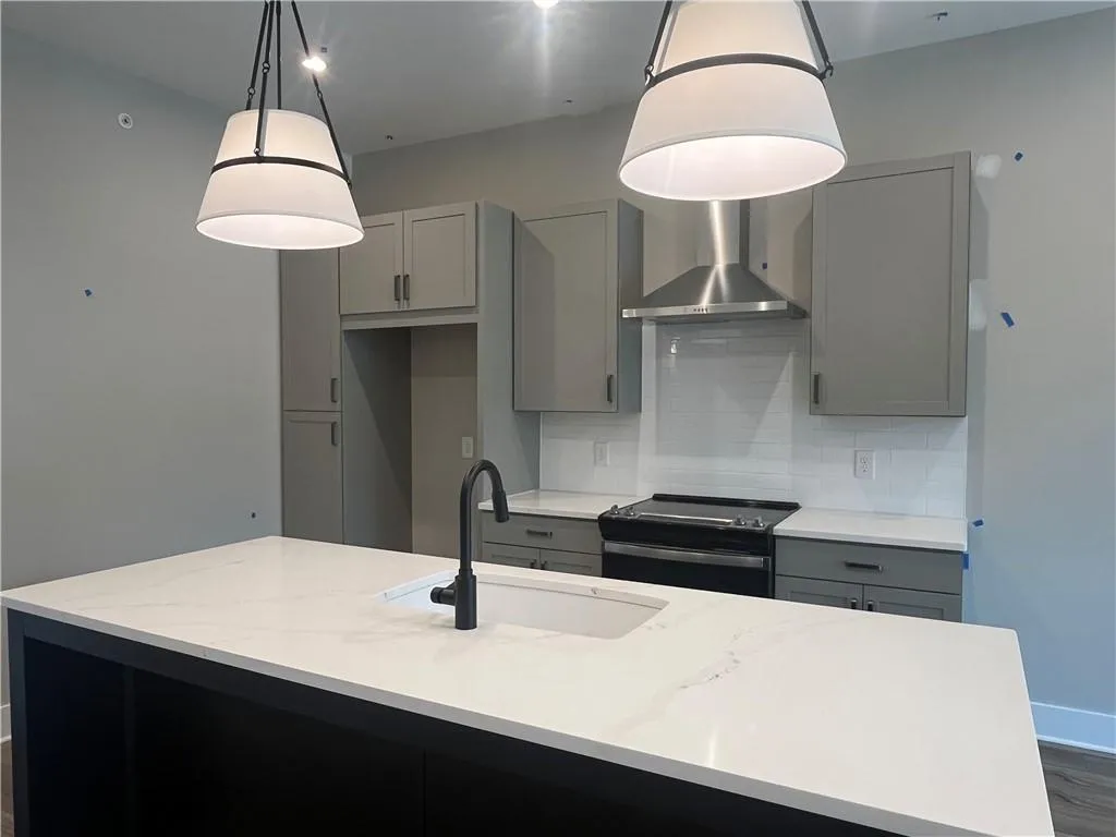 Kitchen featuring gray cabinetry, black electric range, wall chimney range hood, an island with sink, and decorative backsplash