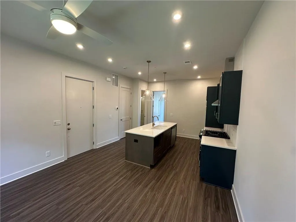 Kitchen featuring an island with sink, dark wood-style flooring, recessed lighting, hanging light fixtures, and dark brown cabinets