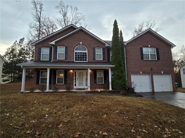 Brick exterior with a covered porch featuring columns, an arched window, and a two-car garage