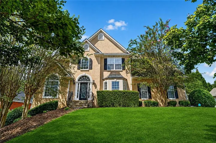 Stucco exterior featuring multiple gables, arched entry with transom window, bay window, and manicured lawn