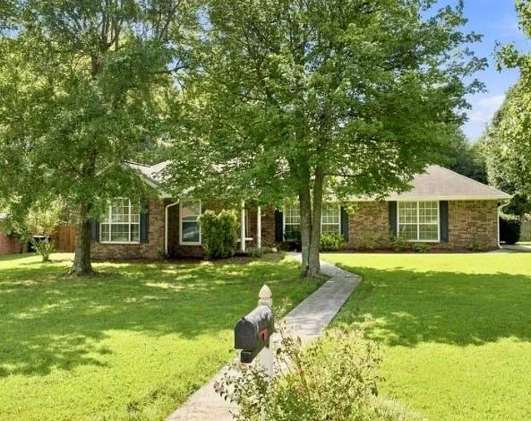 Brick exterior, mature trees, concrete pathway, gabled roofline, front yard