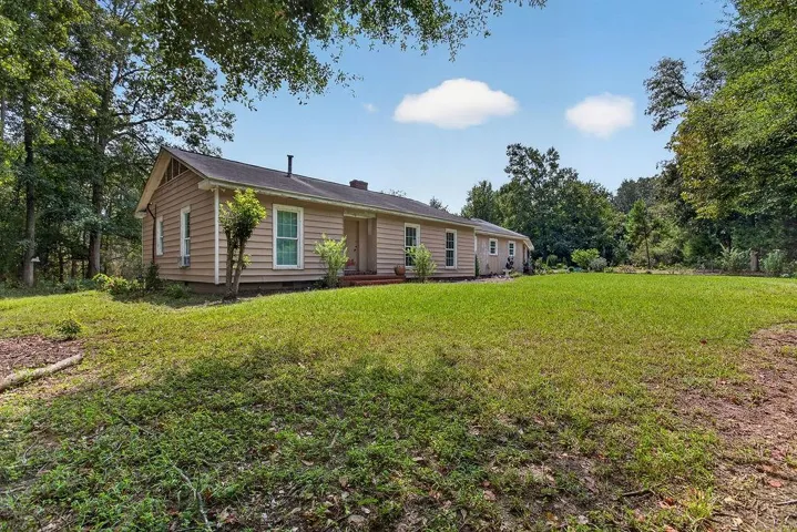 Expansive green lawn with mature trees and a single-story residence featuring horizontal siding and multiple windows