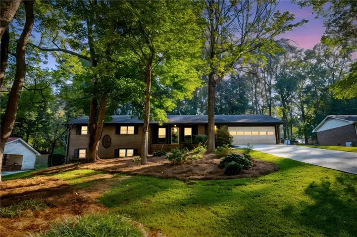 Brick exterior with a prominent two-car garage, mature trees, and a concrete driveway