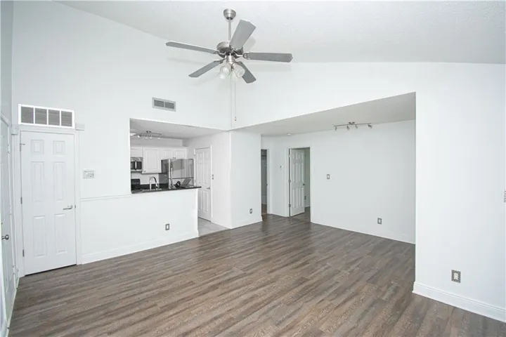 Vaulted ceiling with a ceiling fan, wood-finish flooring, white kitchen cabinetry with stainless steel appliances, and a breakfast bar