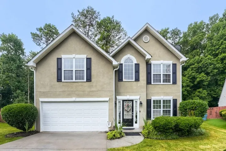 Two-story stucco exterior with gabled roof lines, attached two-car garage, arched entry window, and mature landscaping