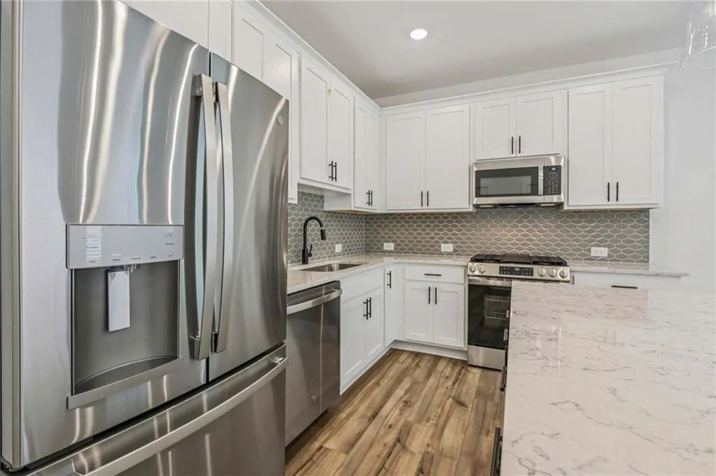 Kitchen featuring appliances with stainless steel finishes, wood finished floors, white cabinetry, decorative backsplash, and light stone countertops