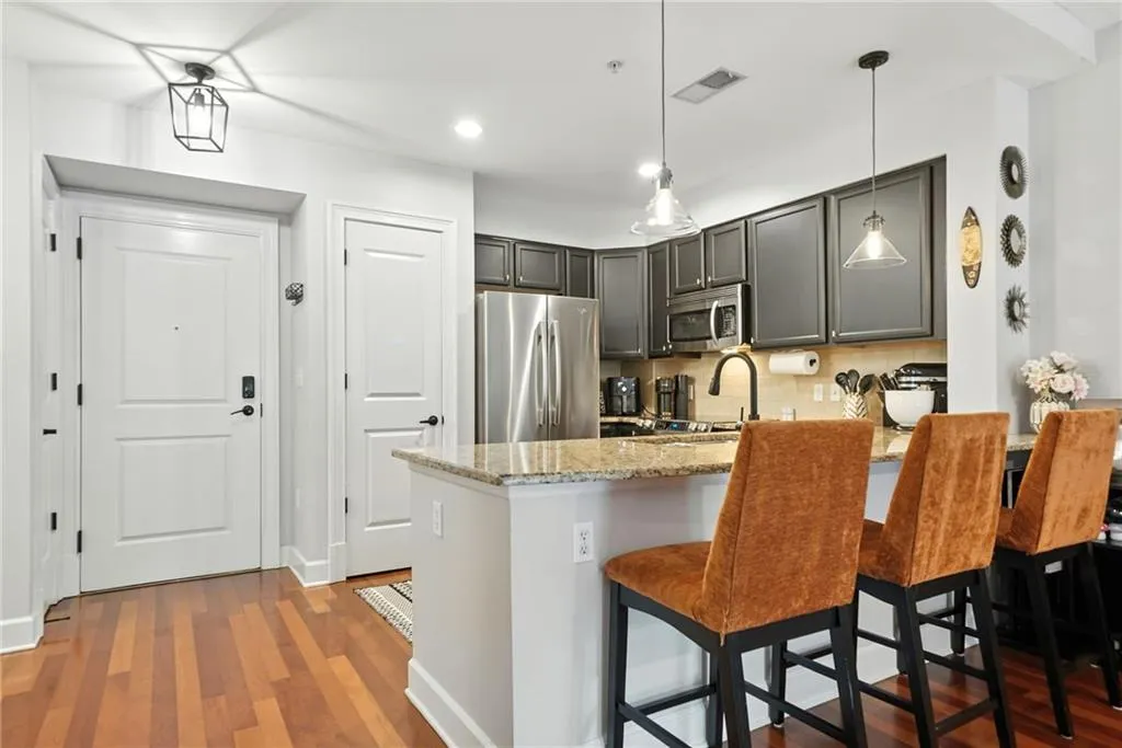 Kitchen with wood finished floors, decorative backsplash, a peninsula, light stone counters, and appliances with stainless steel finishes