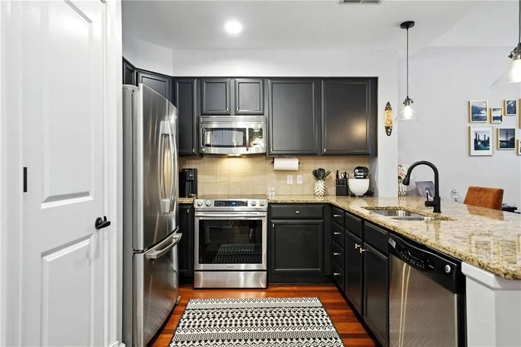 Kitchen with stainless steel appliances, dark wood-style floors, backsplash, light stone counters, and a peninsula