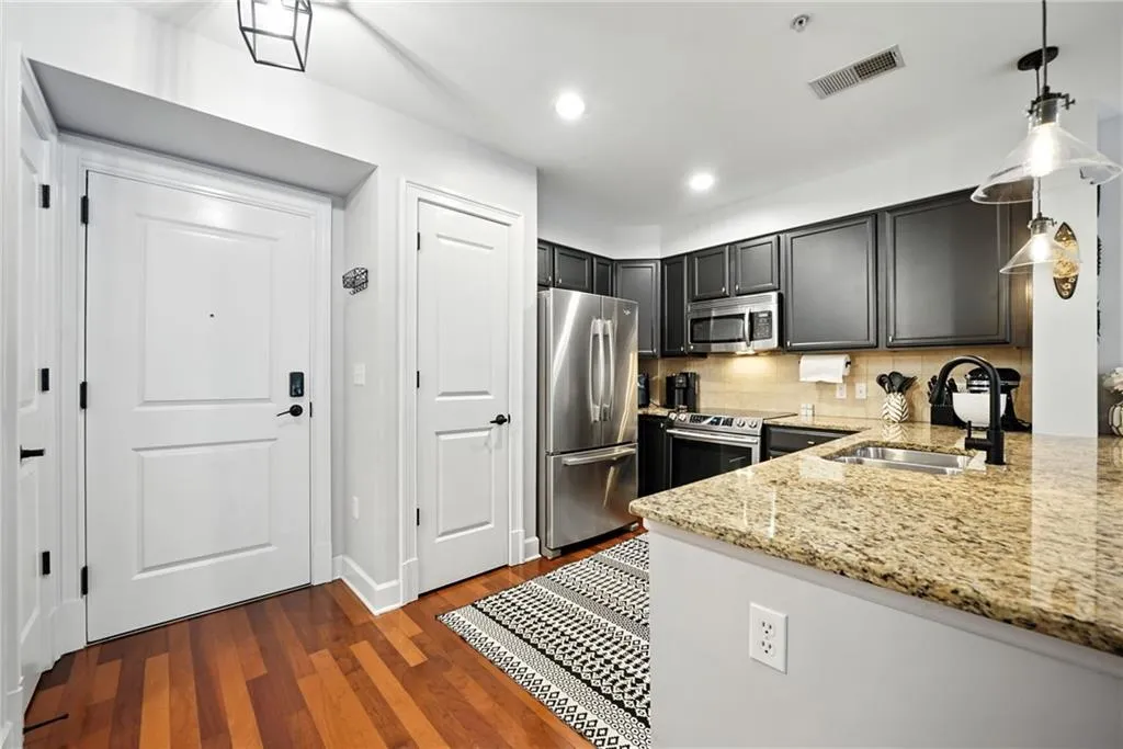 Kitchen featuring backsplash, stainless steel appliances, light stone counters, dark wood-style floors, and recessed lighting