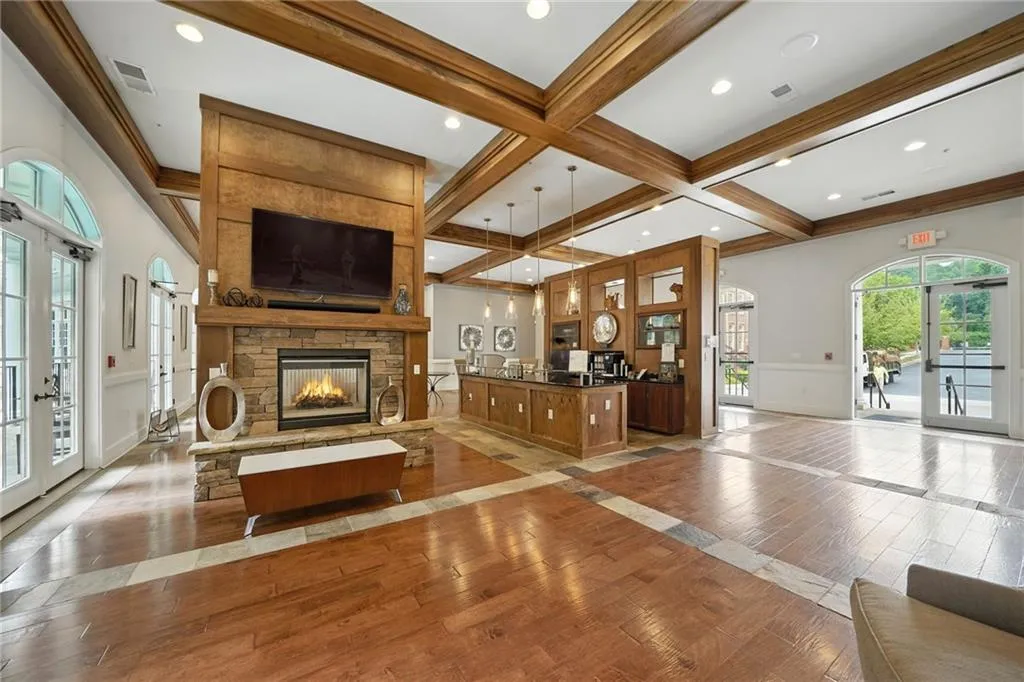 Living area with coffered ceiling, light wood finished floors, beam ceiling, french doors, and a stone fireplace