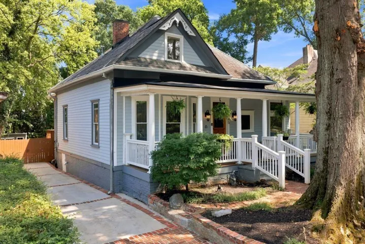 Charming exterior featuring a covered porch with white railings, a brick-edged driveway, and a prominent chimney