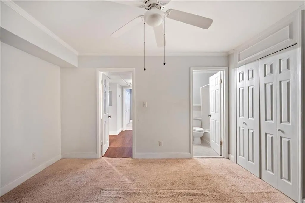 Unfurnished bedroom with carpet floors, ornamental molding, ensuite bath, and a ceiling fan