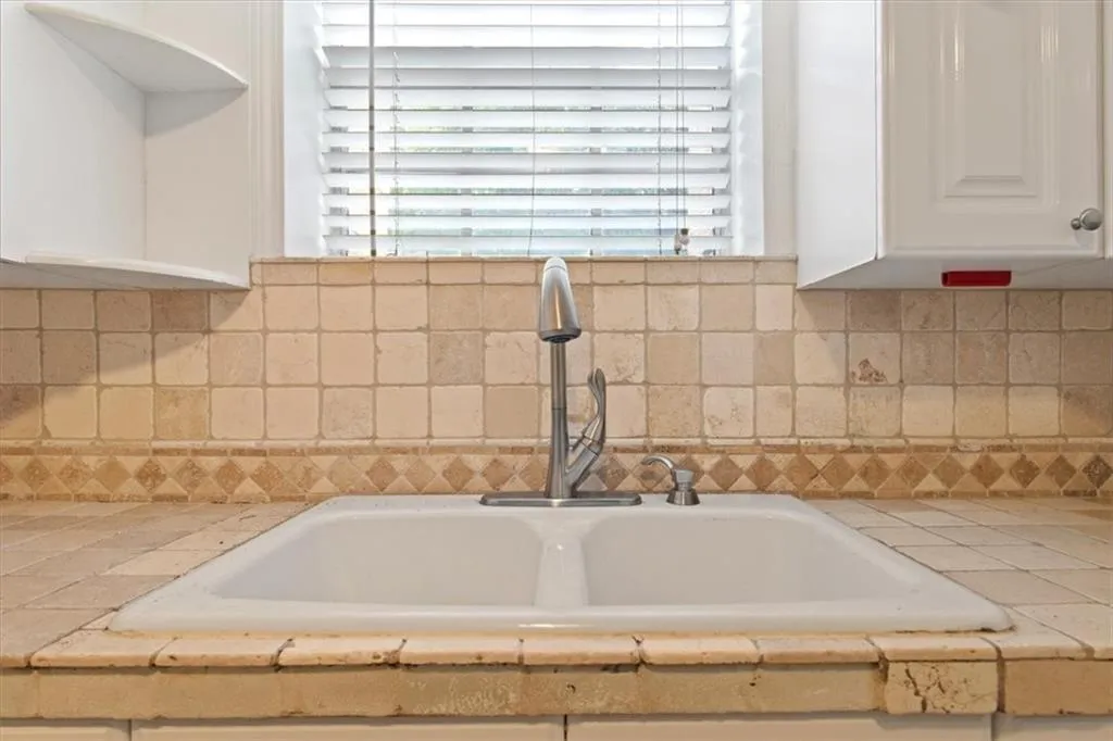 Kitchen view of white cabinetry, decorative backsplash, and tile counters