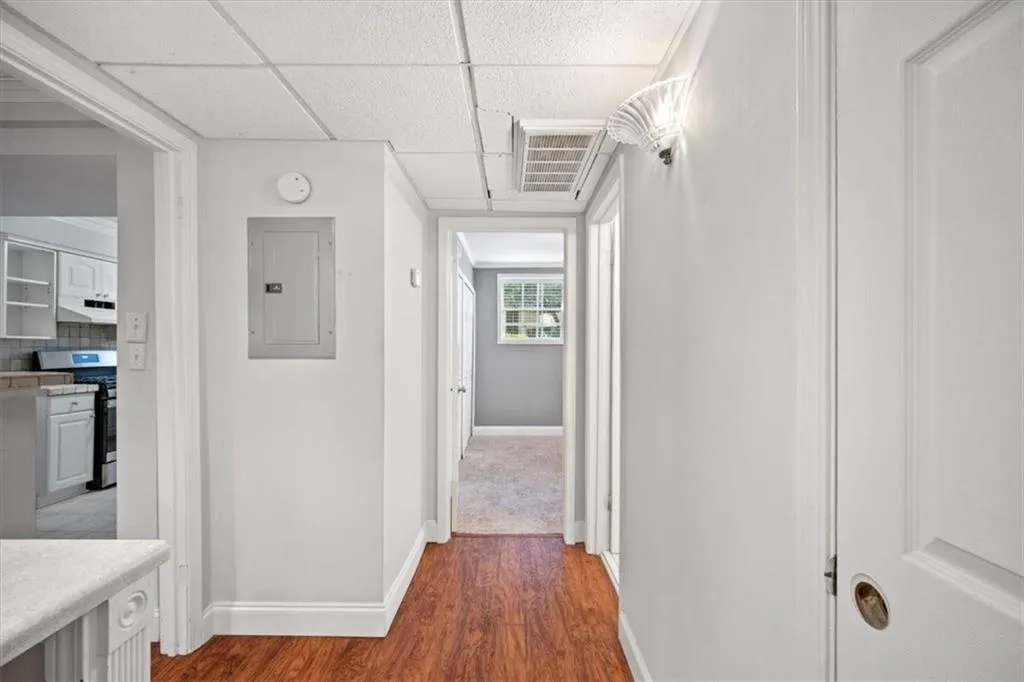 Corridor with electric panel, wood finished floors, and a paneled ceiling