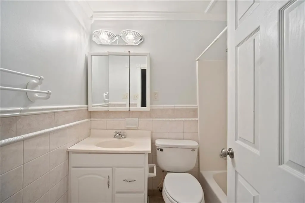Full bath with vanity, crown molding, tile walls, washtub / shower combination, and a wainscoted wall