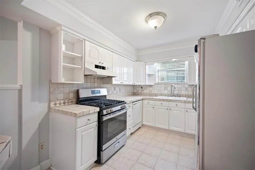 Kitchen featuring white appliances, under cabinet range hood, open shelves, white cabinets, and crown molding
