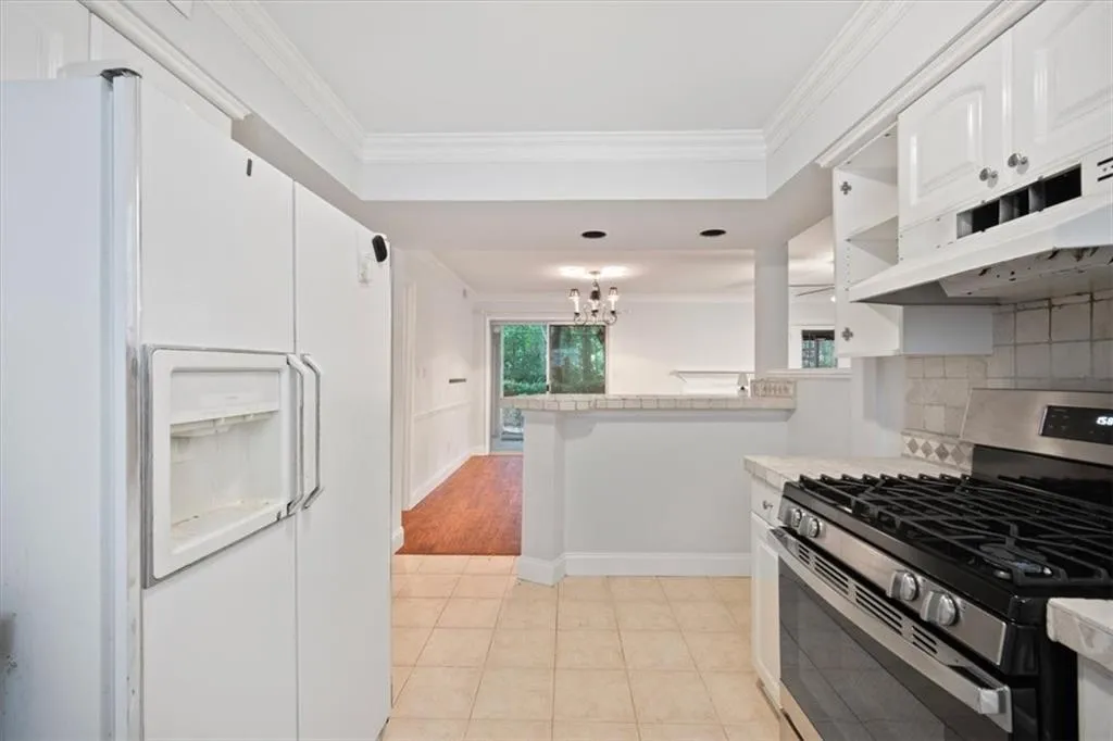 Kitchen with stainless steel gas stove, white fridge with ice dispenser, crown molding, backsplash, and under cabinet range hood