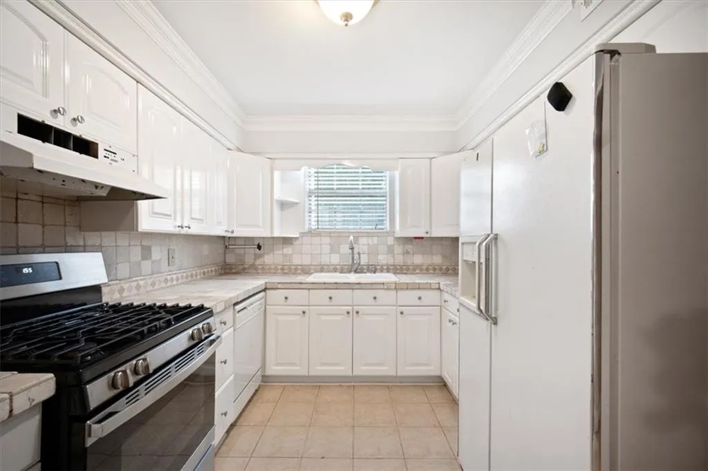 Kitchen featuring white appliances, under cabinet range hood, light countertops, light tile patterned flooring, and crown molding