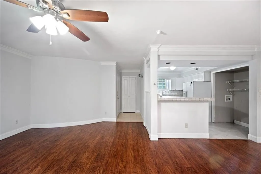 Unfurnished living room with ceiling fan, wood finished floors, and ornamental molding