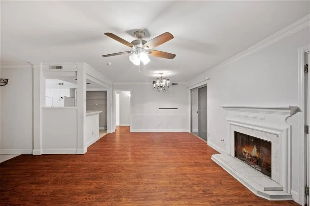 Unfurnished living room featuring ceiling fan, a fireplace, a chandelier, crown molding, and wood finished floors