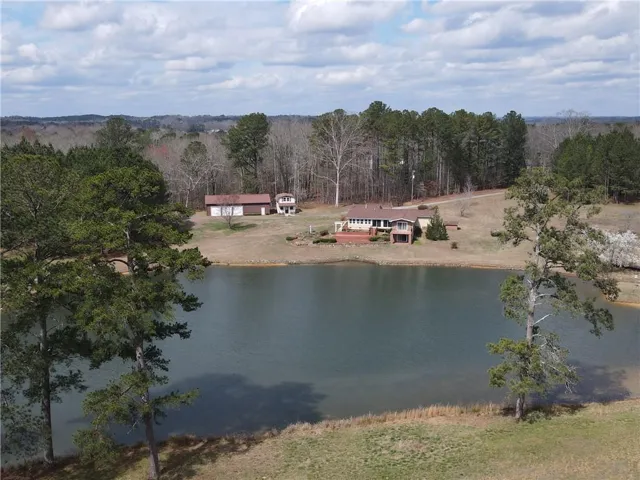 Property with private pond frontage, featuring a multi-level residence with an expansive deck, a detached garage, and a separate outbuilding