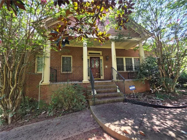 Brick facade residence featuring a covered front porch with white columns, a dark wood entry door with ornate glass, and black wrought iron railings