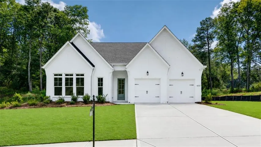 White exterior with a dark roof, dual garage doors, a light green front door, and a concrete driveway