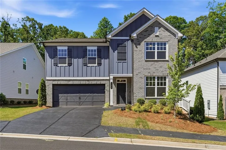 Two-story residence featuring a brick and board-and-batten facade, an attached two-car garage, multiple windows with dark shutters, and a covered entry