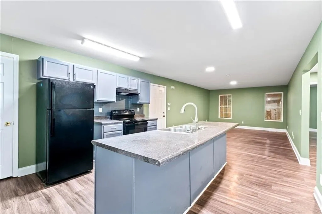 Kitchen featuring black appliances, light wood-type flooring, a center island with sink, decorative backsplash, and under cabinet range hood