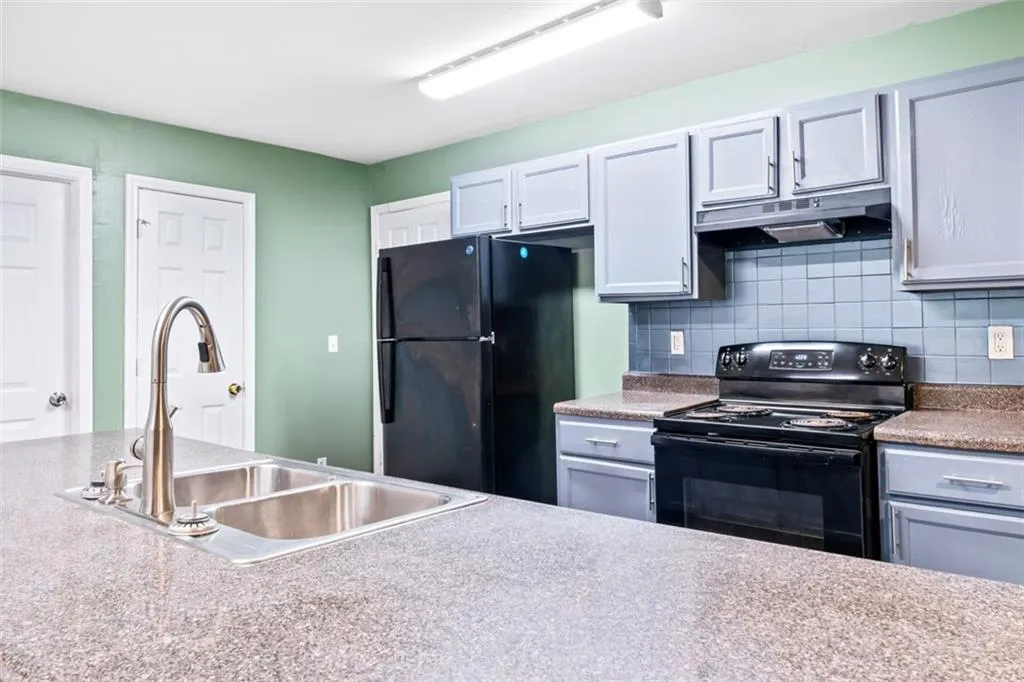 Kitchen with black appliances, under cabinet range hood, and decorative backsplash