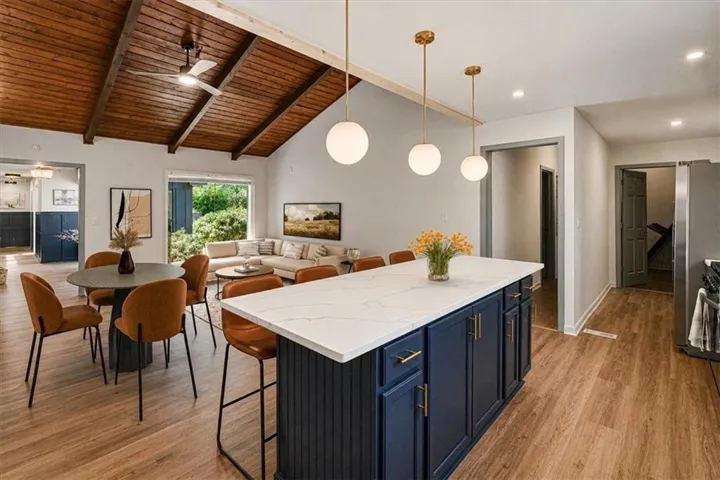 Open-concept living space featuring a vaulted wood-finish ceiling, wood-finish flooring, a kitchen island with a quartz countertop, and a dining area