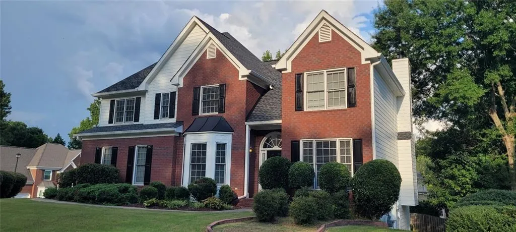 Brick and siding exterior with dark shutters, multiple gables, and a prominent bay window