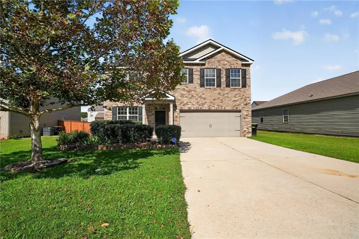 Brick facade residence featuring a two-car garage, concrete driveway, front lawn, and established landscaping