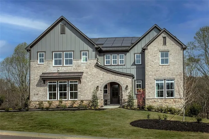 Brick and board-and-batten exterior with an arched entryway, multiple windows, and a paved driveway leading to the entrance