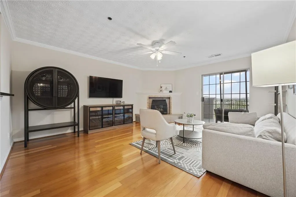 Living room with light wood-style floors, ceiling fan, a glass covered fireplace, visible vents, and crown molding