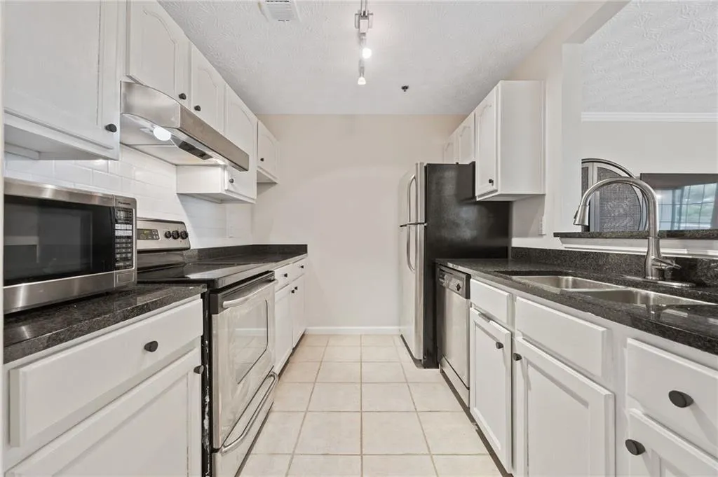Kitchen with a sink, stainless steel appliances, under cabinet range hood, dark stone countertops, and visible vents