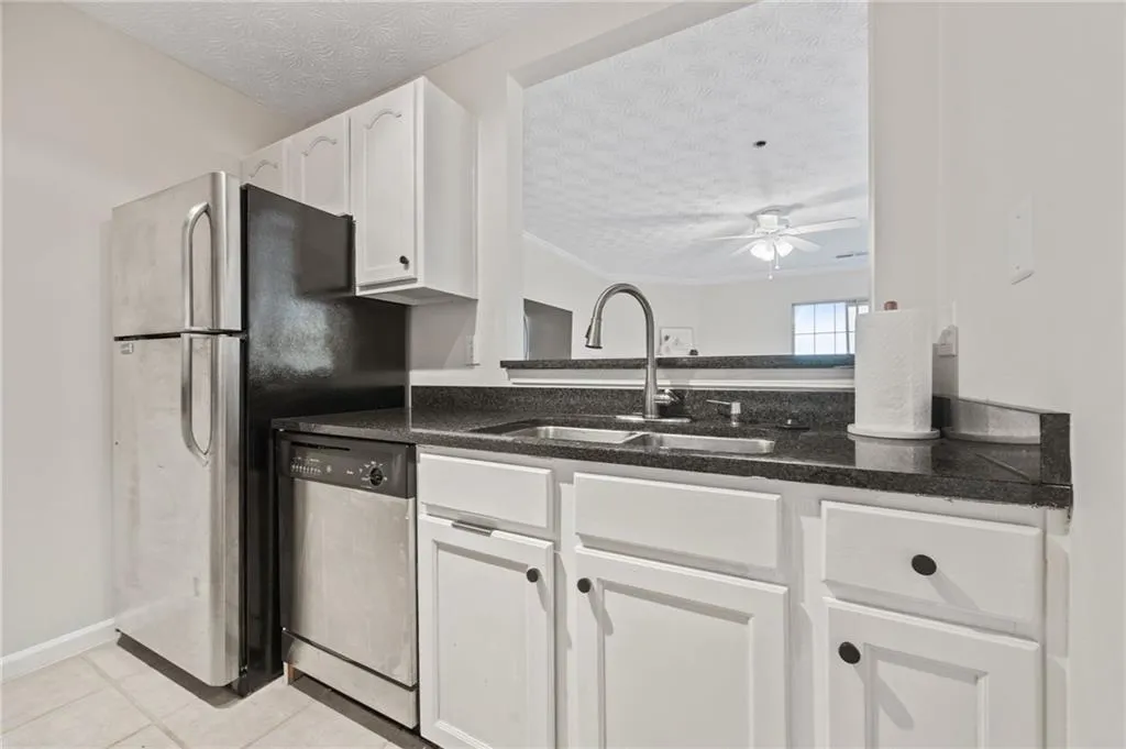 Kitchen with a sink, a ceiling fan, white cabinetry, stainless steel dishwasher, and a textured ceiling