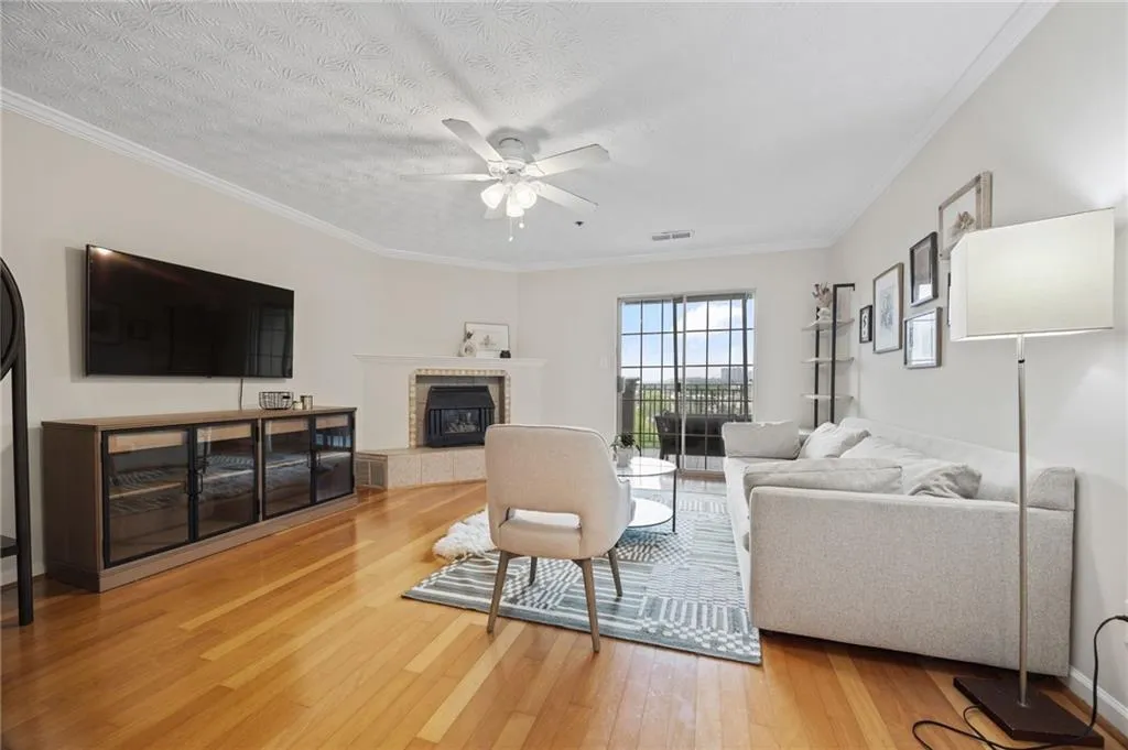 Living room featuring a fireplace, ceiling fan, crown molding, visible vents, and wood finished floors