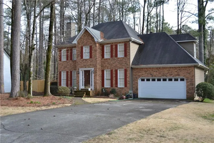 Colonial-style house with concrete driveway, a garage, a chimney, and brick siding