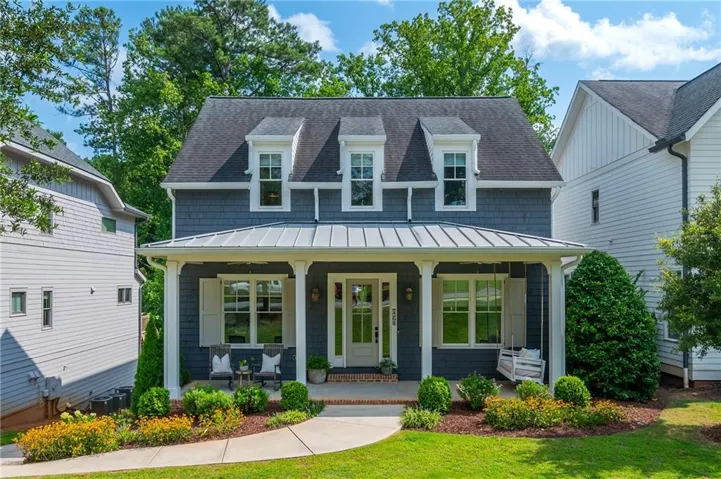 Shingle-sided residence featuring a covered front porch with white columns, dormer windows, and a metal awning