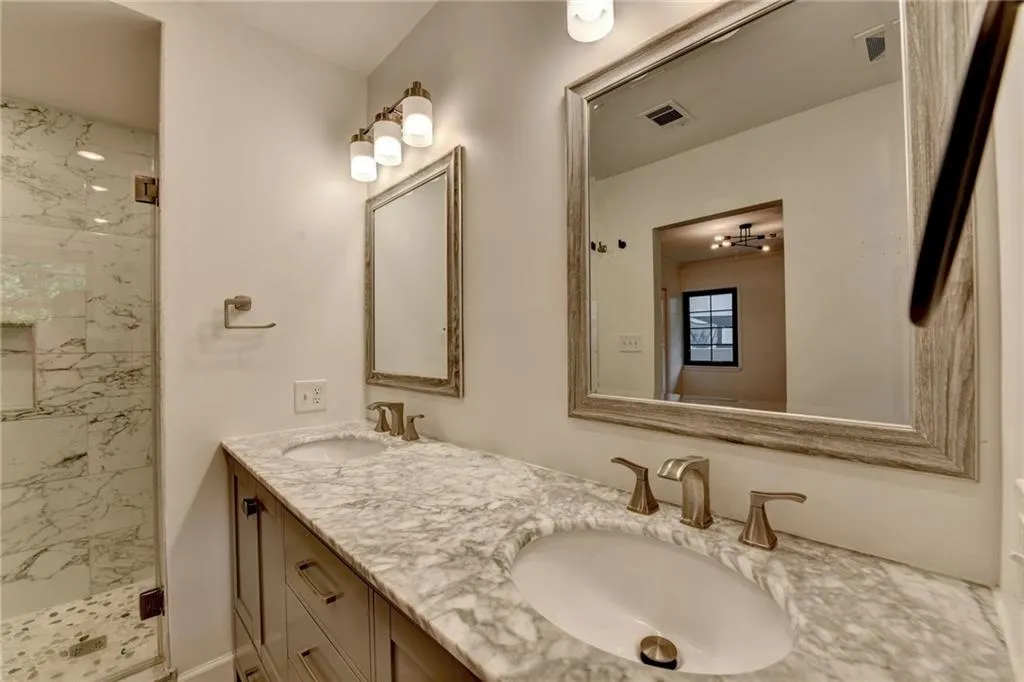 Bathroom featuring a marble finish shower, double vanity, and marble look tile flooring