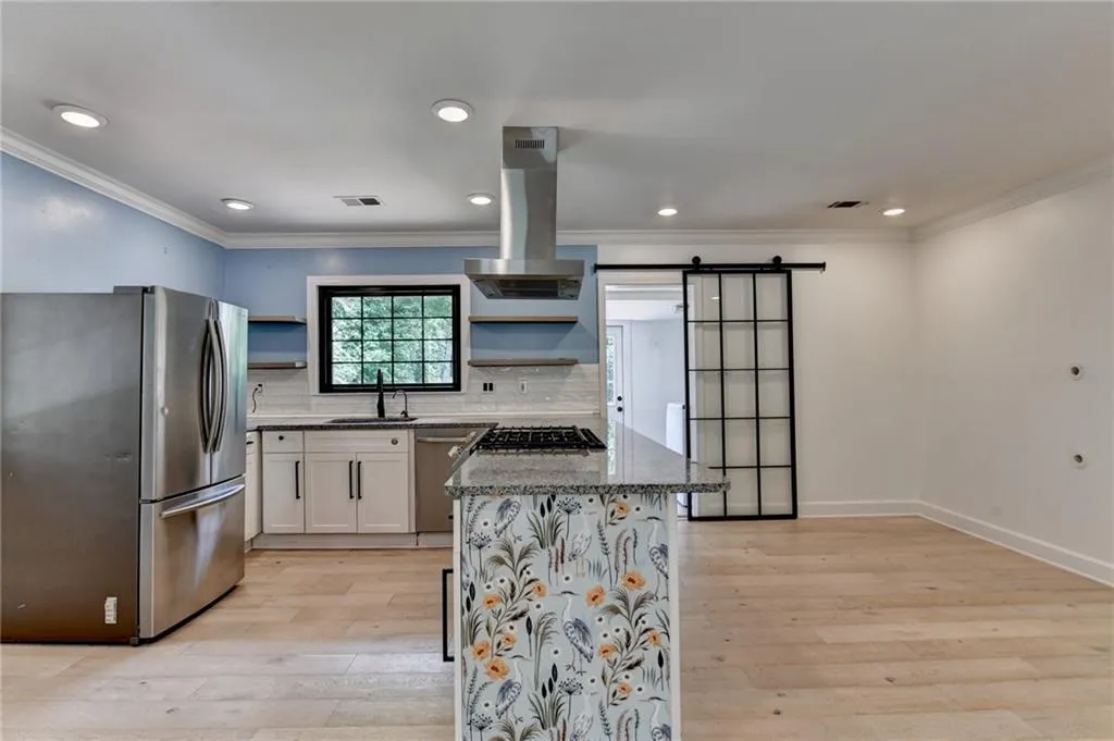 Kitchen with appliances with stainless steel finishes, open shelves, island exhaust hood, dark stone counters, and crown molding