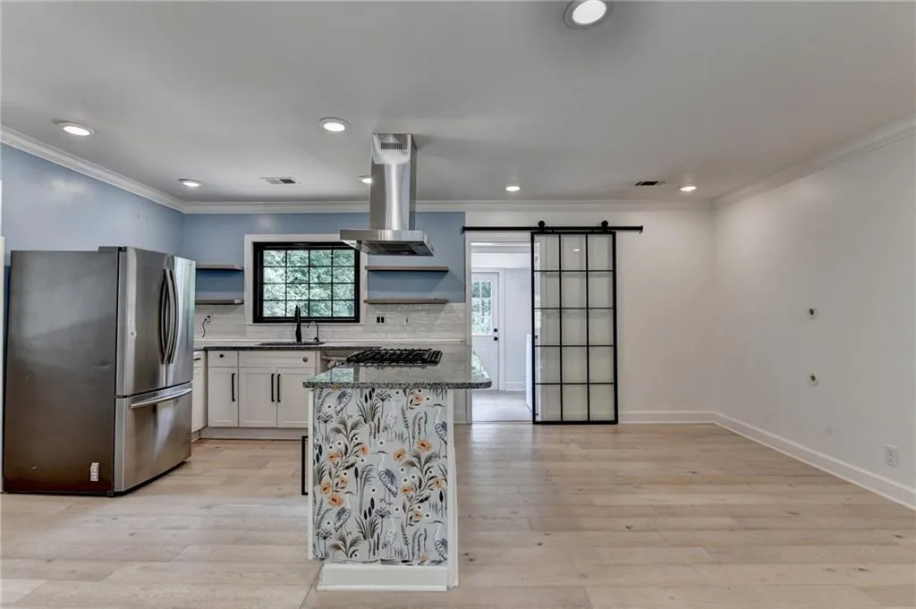 Kitchen with freestanding refrigerator, open shelves, island range hood, a barn door, and white cabinets